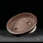 Brown oval pot tilted to show two drainage holes in its interior