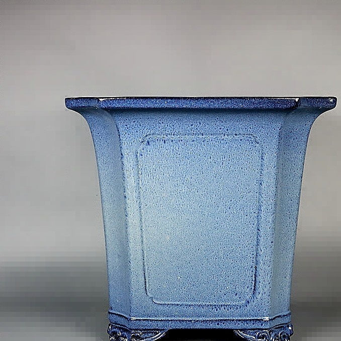Front view of the tall blue-glazed square pot with dark rim and curled feet