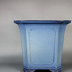 Front view of the tall blue-glazed square pot with dark rim and curled feet