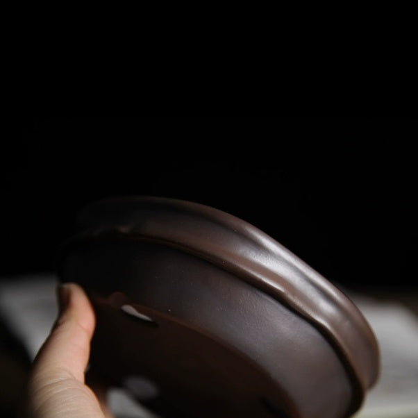 Side view of dark brown irregular pot showing curved rim