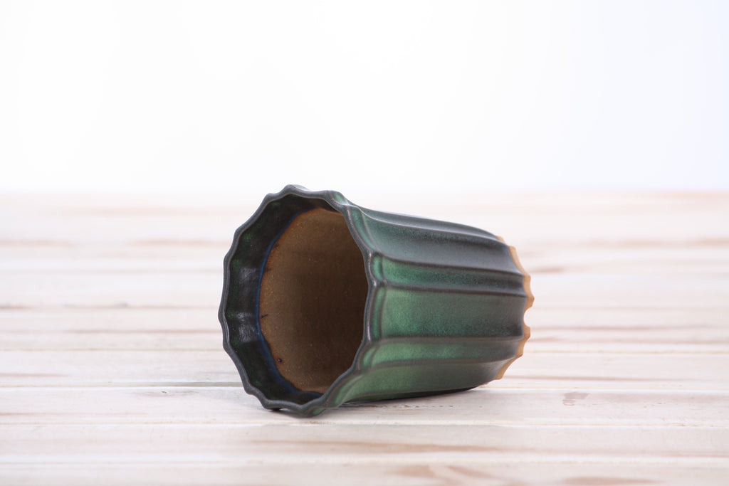 The dark green tall fluted bonsai pot lying on its side to show the opening and fluted walls