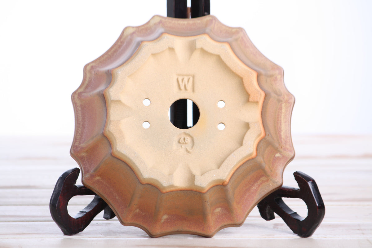 Underside of the warm tan-brown flower-shaped bonsai pot showing a central drainage hole, smaller openings and impressed maker's marks