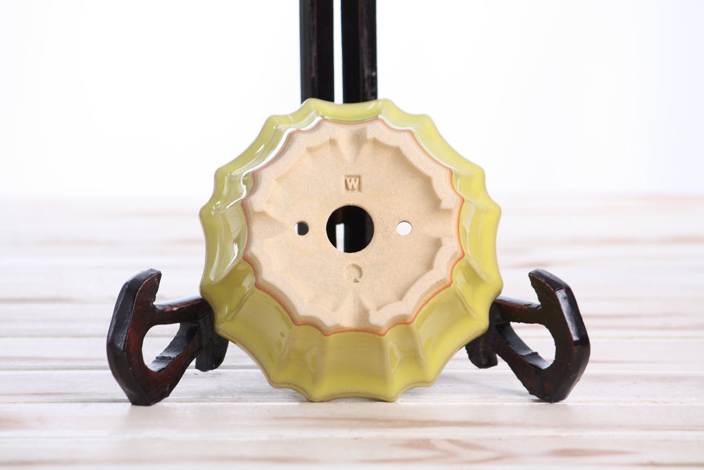 Underside of the yellow flower-shaped bonsai pot showing drainage openings, feet and impressed maker's marks