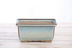 Front view of the pale blue rectangular bonsai pot on a pale wooden surface