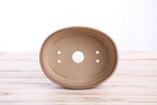 Interior view of the tan-brown oval bonsai pot showing a central drainage hole and four smaller openings