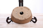 Underside of the tan-brown oval bonsai pot showing a central drainage hole, smaller openings and impressed maker's marks
