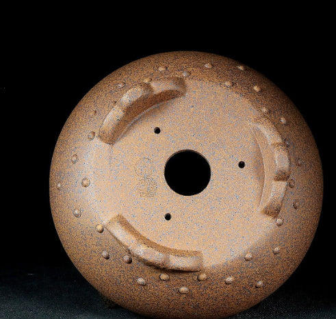 Underside of the brown round pot showing central drainage hole and three smaller openings