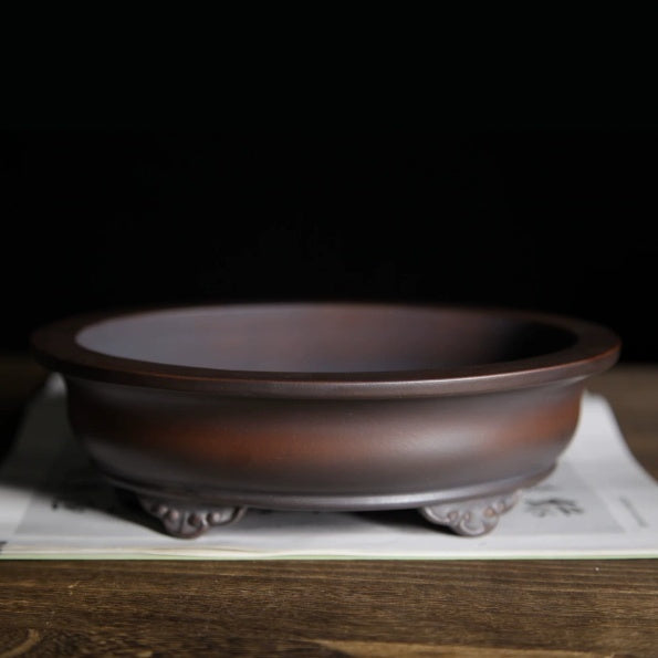 Dark brown oval pot with curled feet and rolled rim