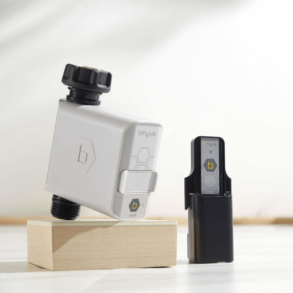 Gray B-hyve hose timer beside a black plug-in hub on a wooden block