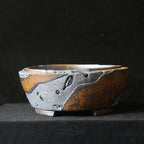 Round bonsai pot with mottled amber surface and raised charcoal patches