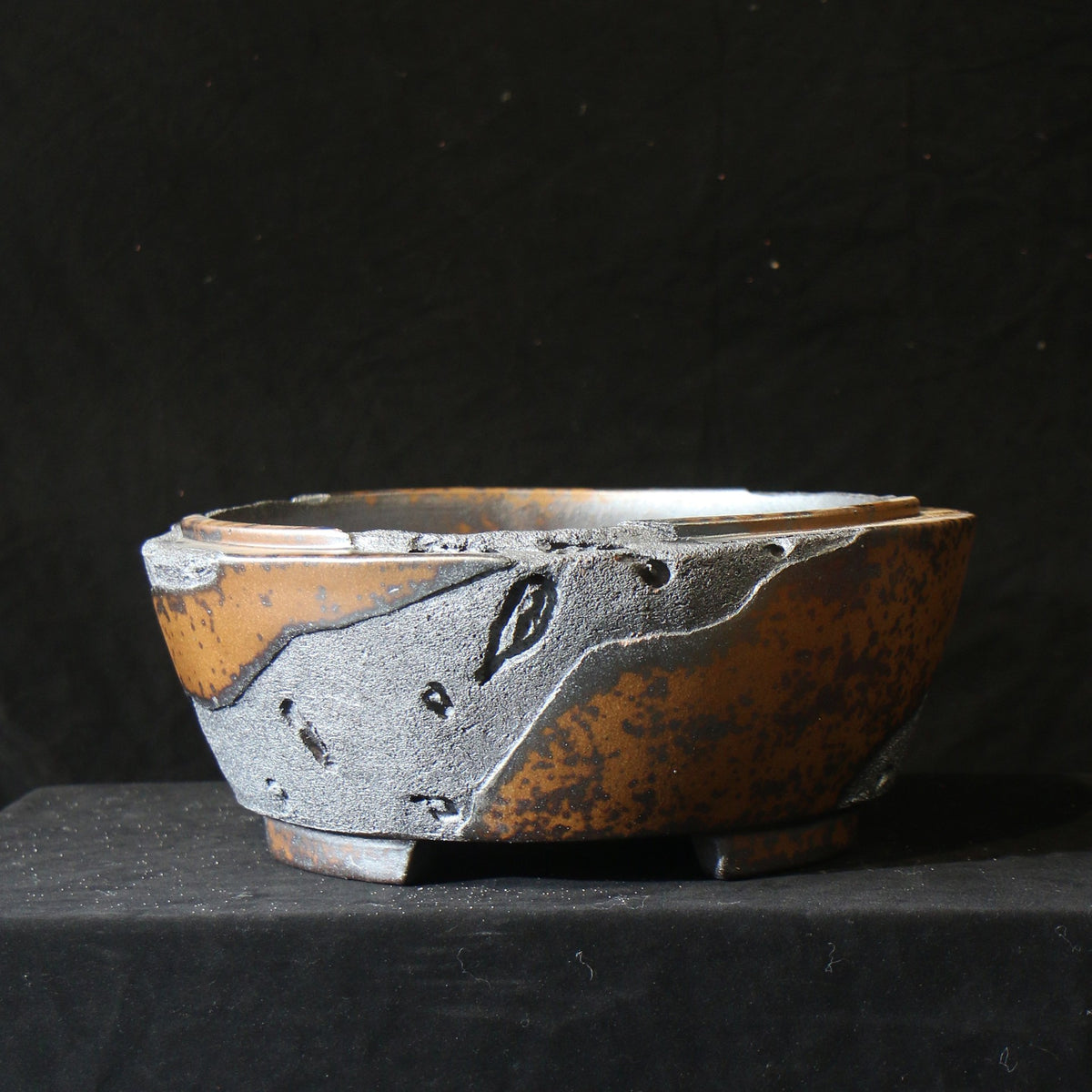 Round bonsai pot with mottled amber surface and raised charcoal patches