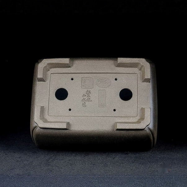 Underside of gray-brown rectangular pot showing two large openings and stamped marks