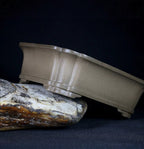 Side profile of taupe rounded rectangular pot tilted on stone