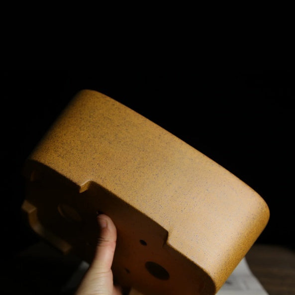 Underside angle of the ochre-glazed pot showing raised feet and drainage openings