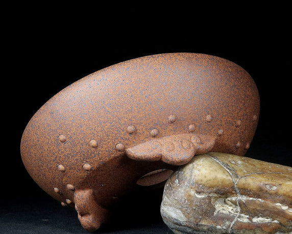 Brown studded round pot tilted on a rock to show its feet
