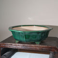 Angled green-glazed pot on a wooden stand showing its pale interior