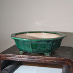 Angled green-glazed pot on a wooden stand showing its pale interior