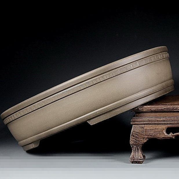 Taupe oval pot with patterned rim band tilted on a wooden stand