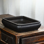 Dark rectangular bonsai pot with rounded walls, raised lip and low feet