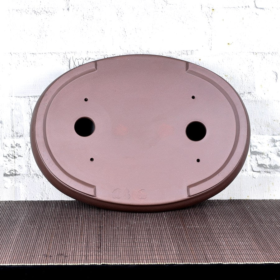 Underside of brown oval bonsai pot showing two large openings and smaller holes