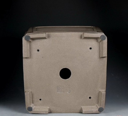 Underside of taupe square pot showing central opening, corner feet and stamped marks