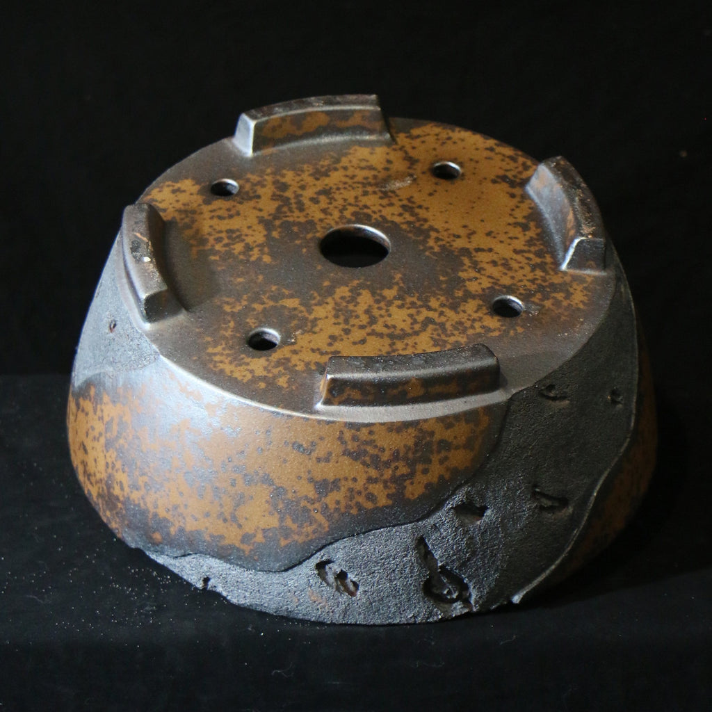 Underside of mottled round pot showing central opening and block feet