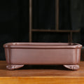 Reddish-brown rectangular purple-clay pot with raised lip and curved decorative feet