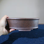 Hand holding mottled brown oval pot to show side profile