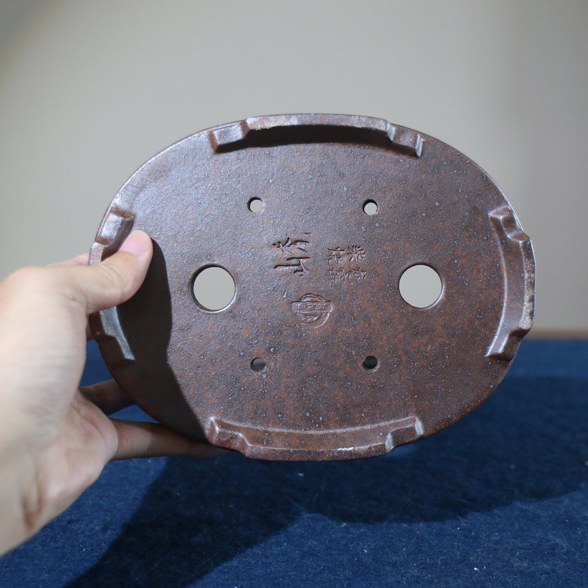 Hand holding underside of brown oval pot showing openings and stamped marks