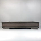 Front view of a long dark brown rectangular bonsai pot with raised rim and short feet