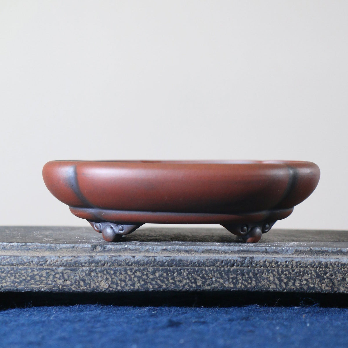 Red-brown lobed bonsai pot with dark accents and curled feet