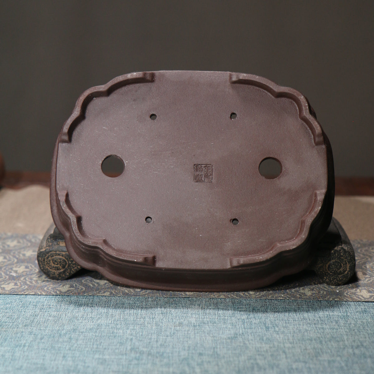Underside of bonsai pot showing drainage holes and low feet