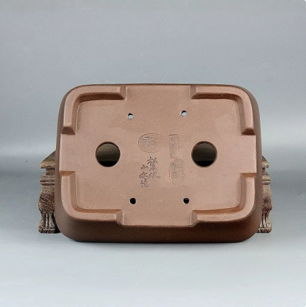 Underside of the brown rectangular pot showing two drainage holes and impressed marks