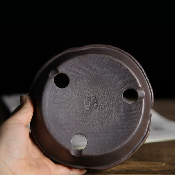 Underside of dark brown irregular pot showing three openings and stamped mark