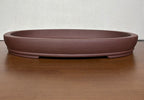Shallow brown oval bonsai pot with a banded base on a wooden table