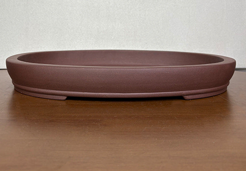 Shallow brown oval bonsai pot with a banded base on a wooden table
