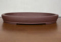 Shallow brown oval bonsai pot with a banded base on a wooden table