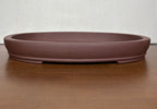 Shallow brown oval bonsai pot with a banded base on a wooden table