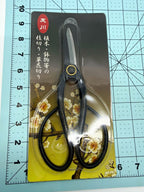 Black long-handled bonsai scissors in clear packaging on a floral backing card