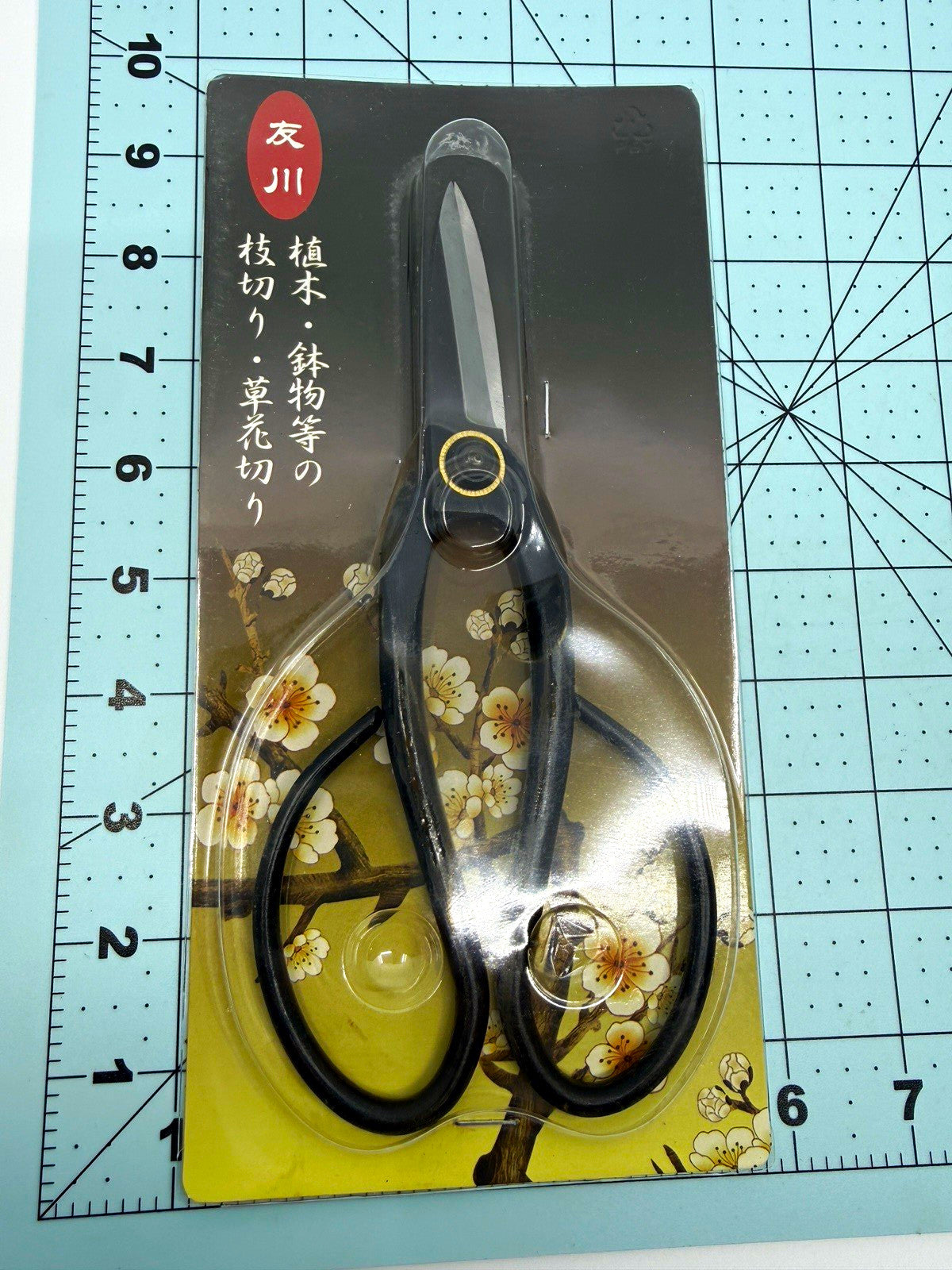 Black long-handled bonsai scissors in clear packaging on a floral backing card