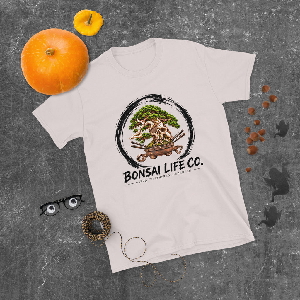 pale gray T-shirt with green bonsai and pirate skull graphic inside a black circle with Bonsai Life Co. lettering, gray flat lay with pumpkins