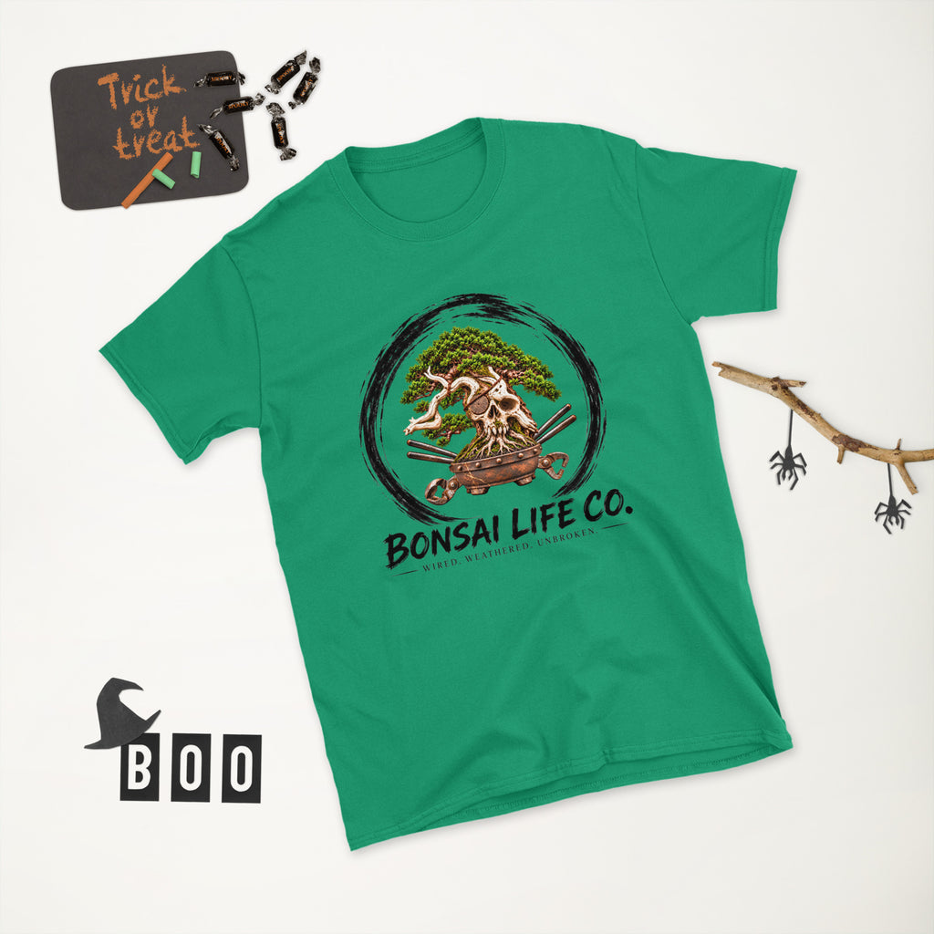bright green T-shirt with green bonsai and pirate skull graphic inside a black circle with Bonsai Life Co. lettering, white Halloween flat lay