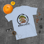 light blue T-shirt with green bonsai and pirate skull graphic inside a black circle with Bonsai Life Co. lettering, gray flat lay with pumpkins