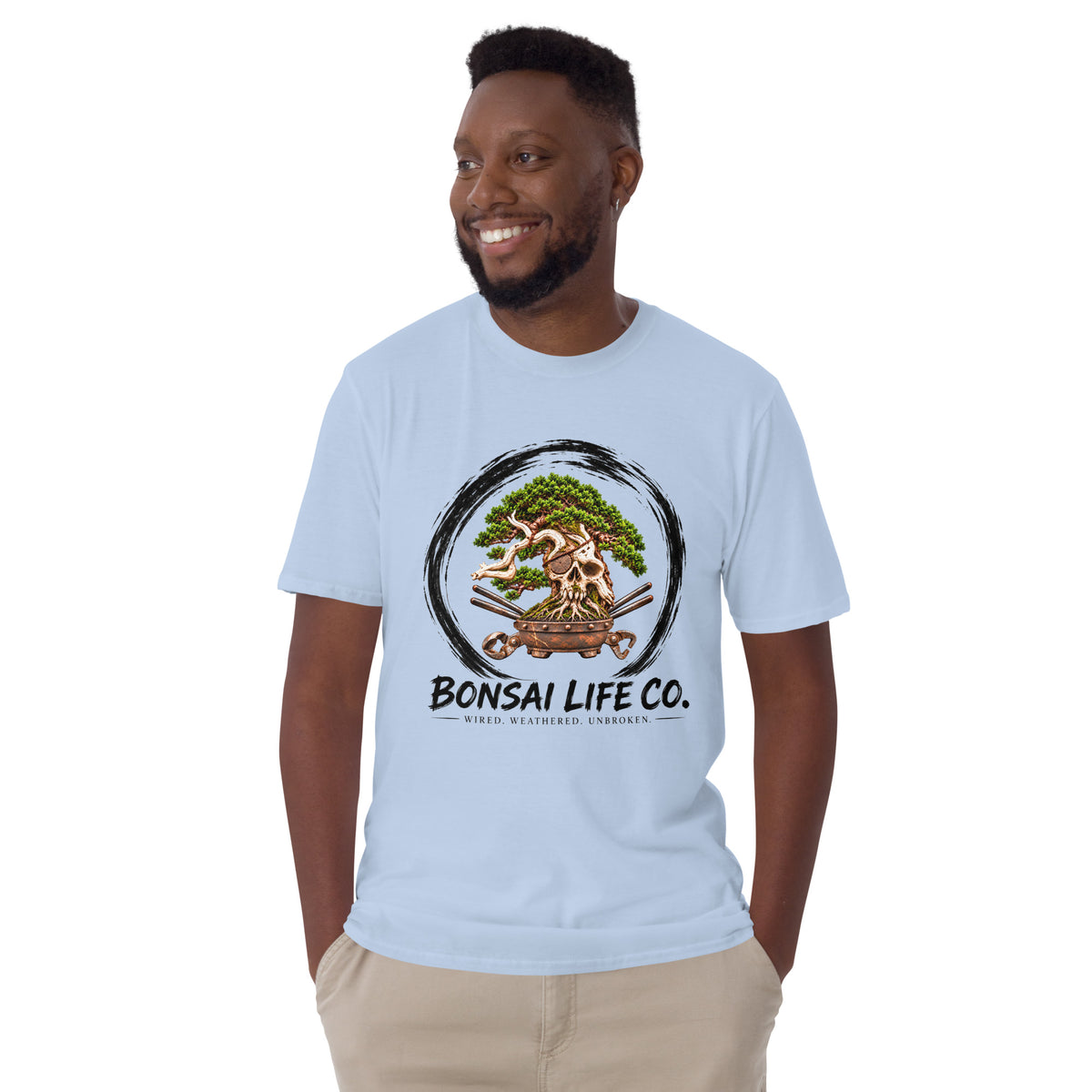 Model wearing light blue T-shirt with green bonsai and pirate skull graphic inside a black circle with Bonsai Life Co. lettering, front view