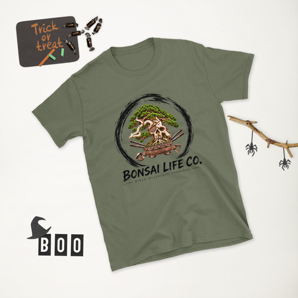 muted olive green T-shirt with green bonsai and pirate skull graphic inside a black circle with Bonsai Life Co. lettering, white Halloween flat lay