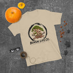 sand beige T-shirt with green bonsai and pirate skull graphic inside a black circle with Bonsai Life Co. lettering, gray flat lay with pumpkins