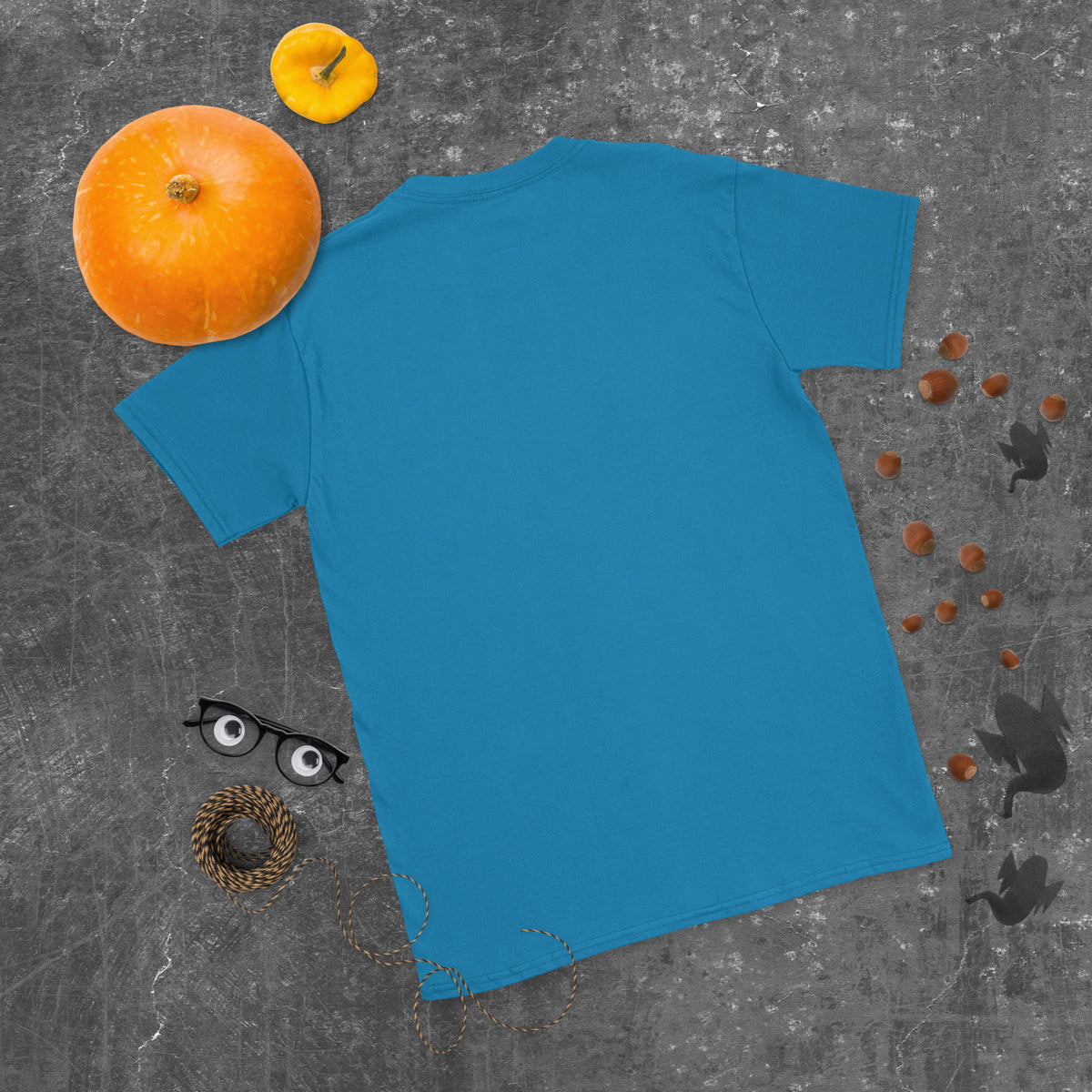 Plain back of sapphire blue Bonsai Life Co. T-shirt in a gray flat lay with pumpkins