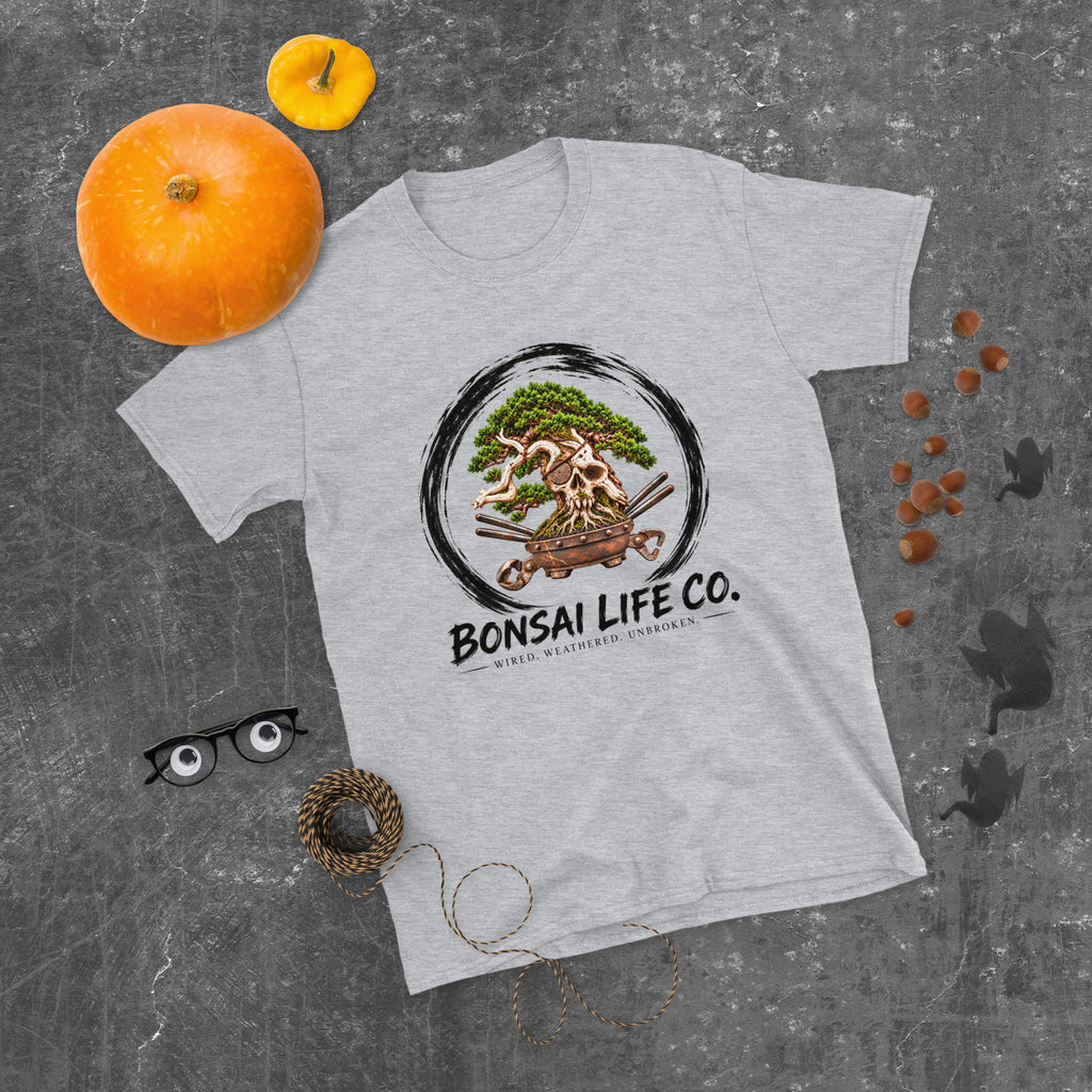 heathered light gray T-shirt with green bonsai and pirate skull graphic inside a black circle with Bonsai Life Co. lettering, gray flat lay with pumpkins