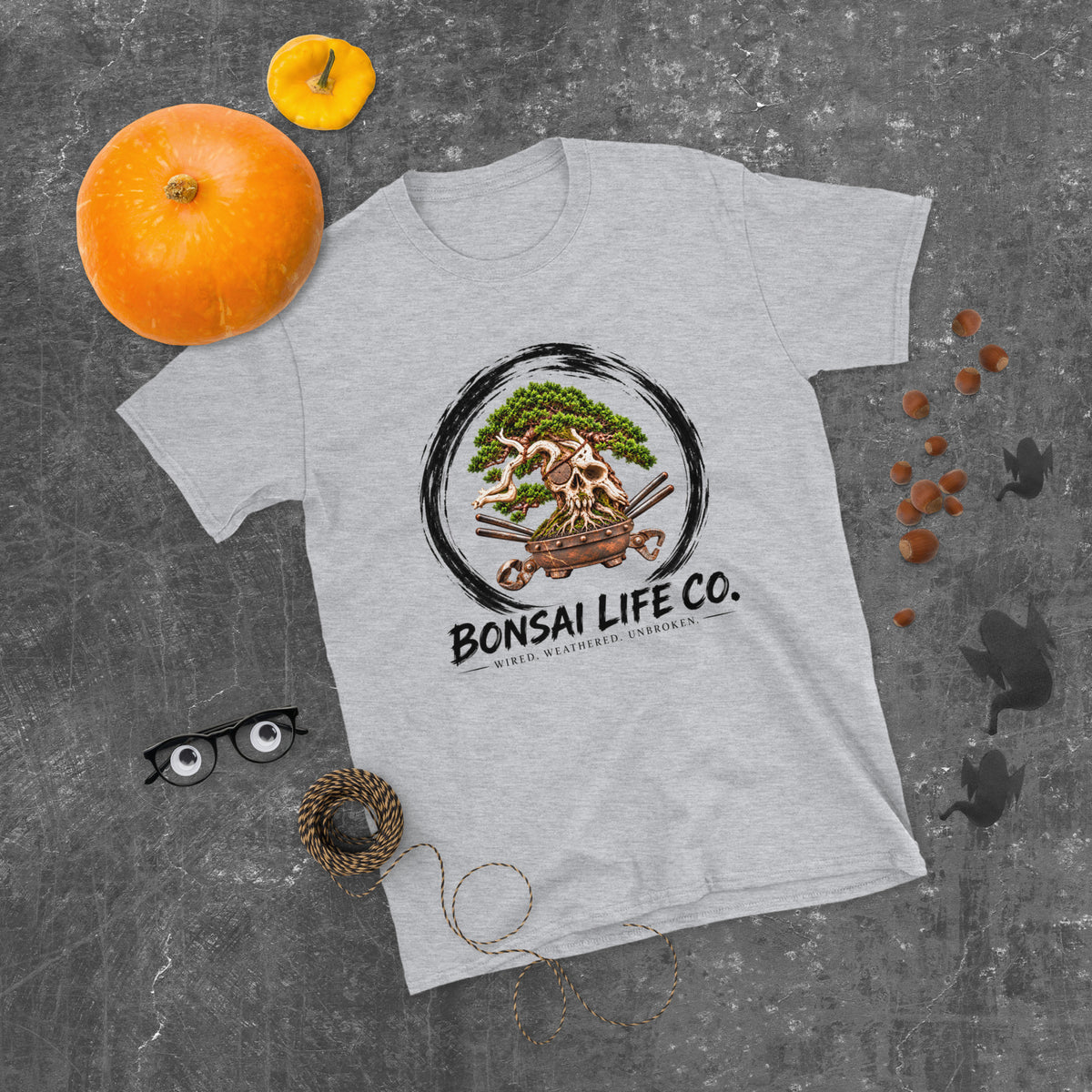heathered light gray T-shirt with green bonsai and pirate skull graphic inside a black circle with Bonsai Life Co. lettering, gray flat lay with pumpkins