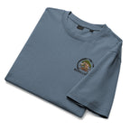 Folded muted blue T-shirt showing small circular bonsai pirate skull chest emblem